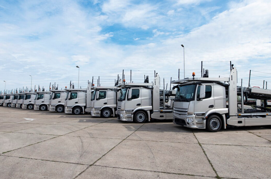 group of trucks parked in line at truck stop, the cloudy blue sky above 