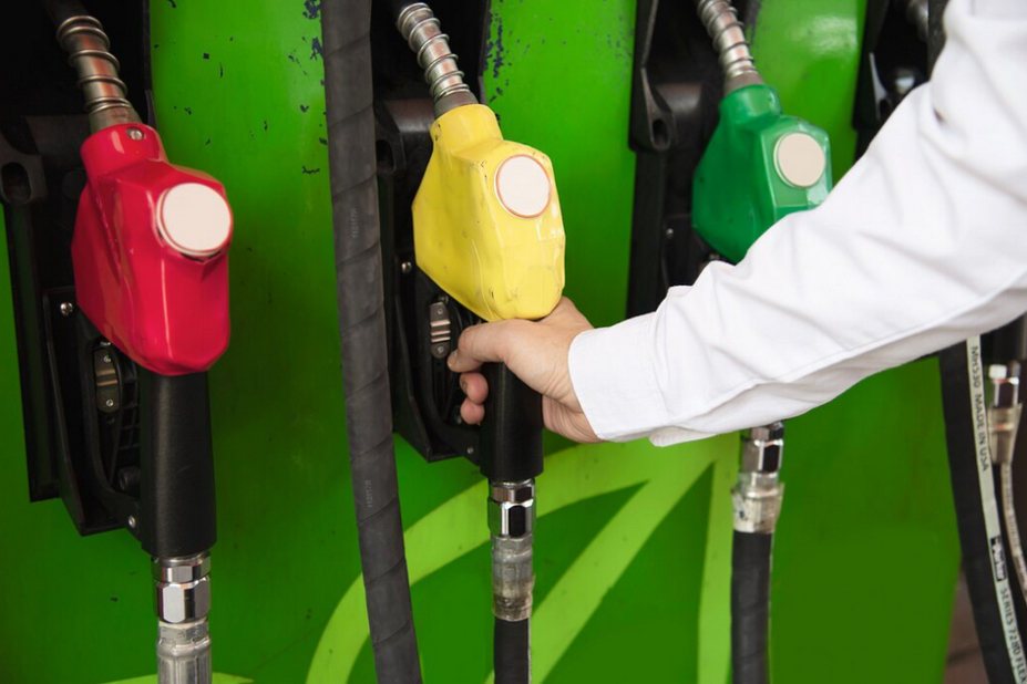 Man putting a yellow gasoline pump nozzle into his car in a pump gas station