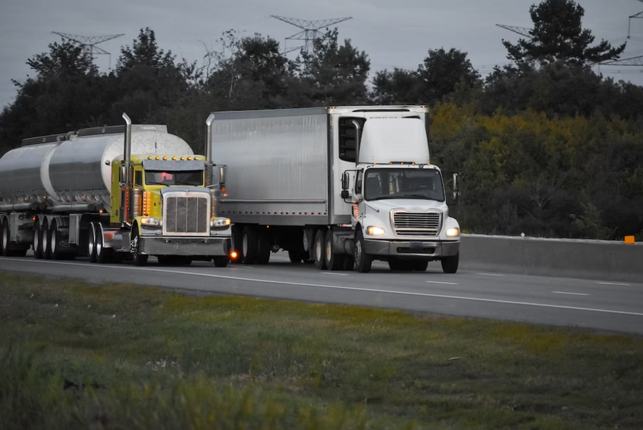 wo silver trucks on the road, the grass and trees on both sides of the road 