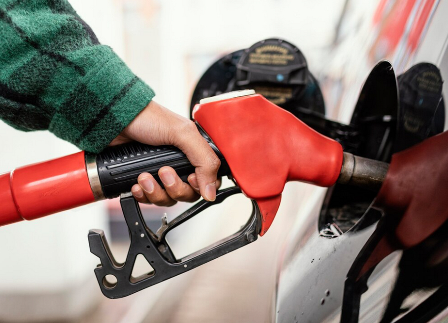A person fueling a car with a red gasoline pump nozzle.