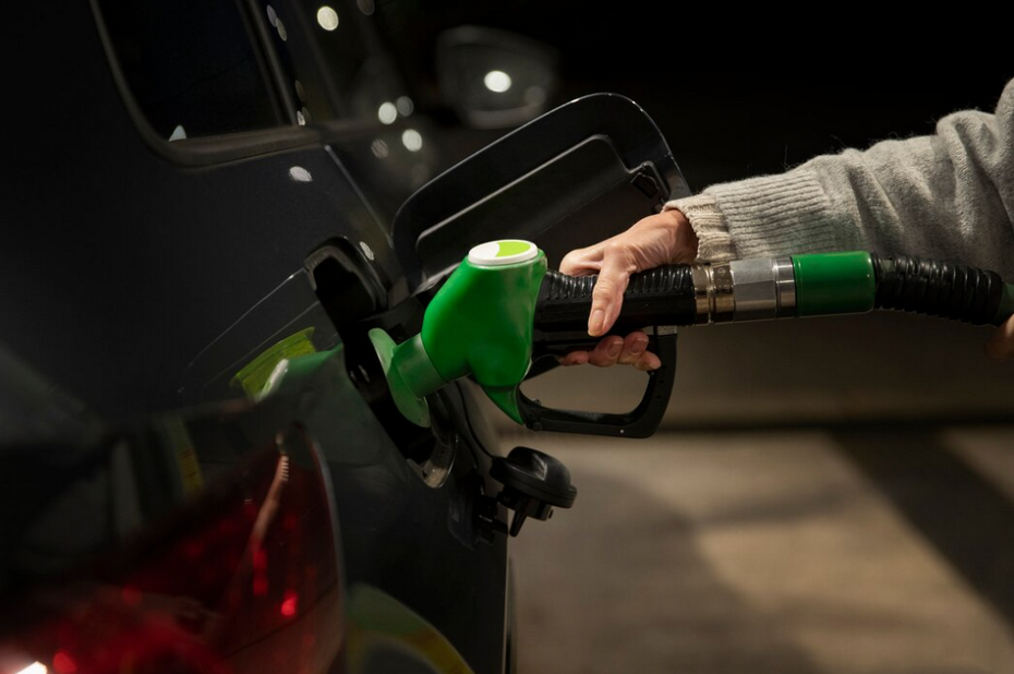 hand is pumping green nozzle into car's fuel tank outside at gas station 
