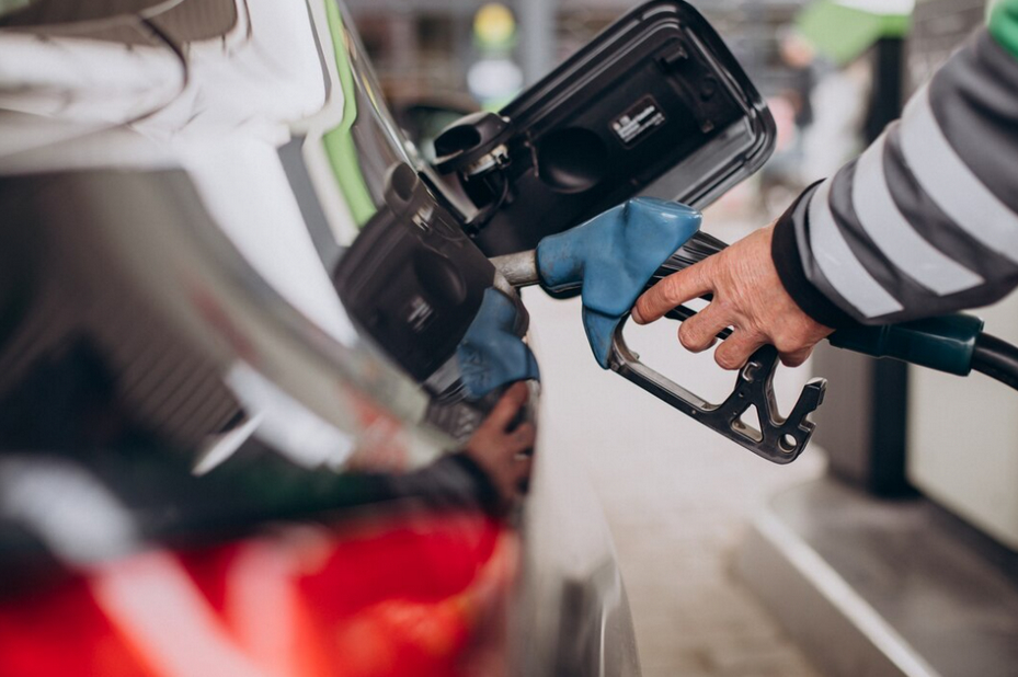 Hand refilling car with fuel, blue glove on nozzle handle