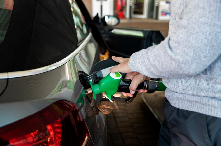A person refueling their car with a green fuel nozzle at a gas station.